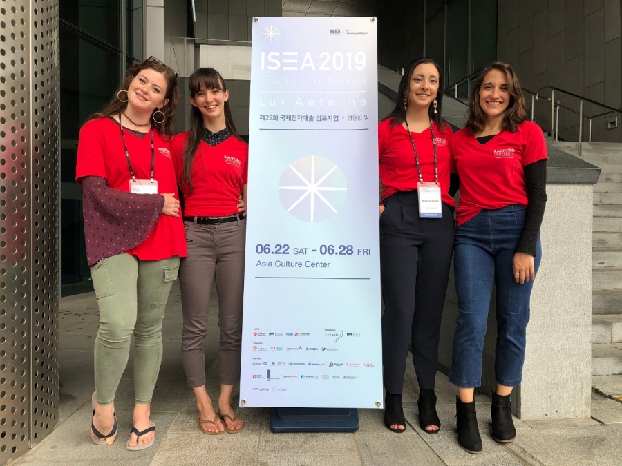 Dance students pose at signage during the 2019 International Symposium on Electronic Art