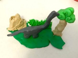 A clay dinosaur eats leave from a clay tree
