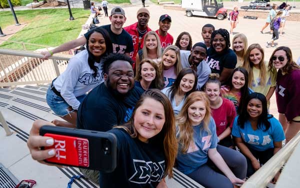 Students wearing their Greek letters pose for a group selfie.