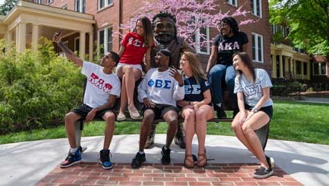 Students in Fraternity and Sorority Life pose for a selfie on the Highlander bench while wearing their respective Greek letters. 