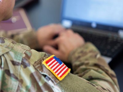 Right arm of a military personnel sitting at computer. Shows American flag patch on right shoulder.