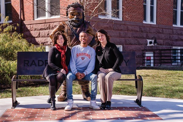 Executive Director for Alumni Relations Laura Turk ’87, M.S. ’90, André Ragsdale and Director of Alumni Relations Sandra M. Bond ’97, MBA ’00, sit on the Highlander Bench near Russell Hall.