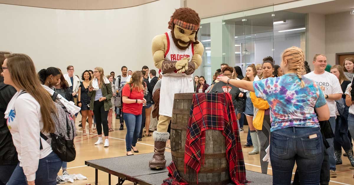 The Highlander watches and cheers as students toss their coins into the barrel.