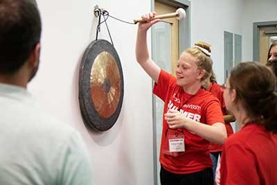 Camper Ellen Jones rings the gong in Torc's break room to celebrate a week of learning at Summer Bridge.