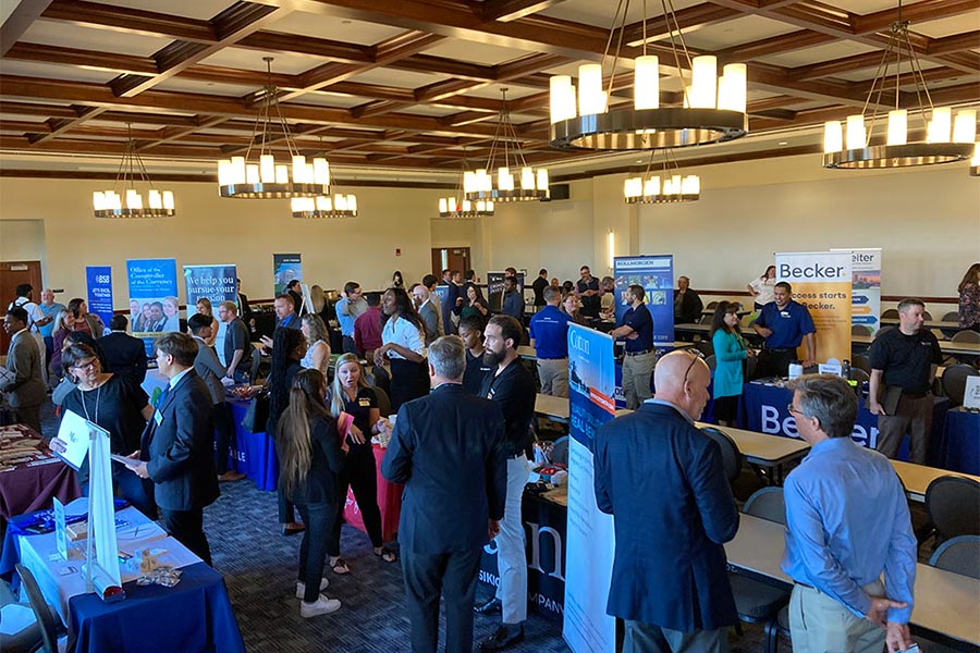 Students and employers mingle at a job fair held in a large conference room.