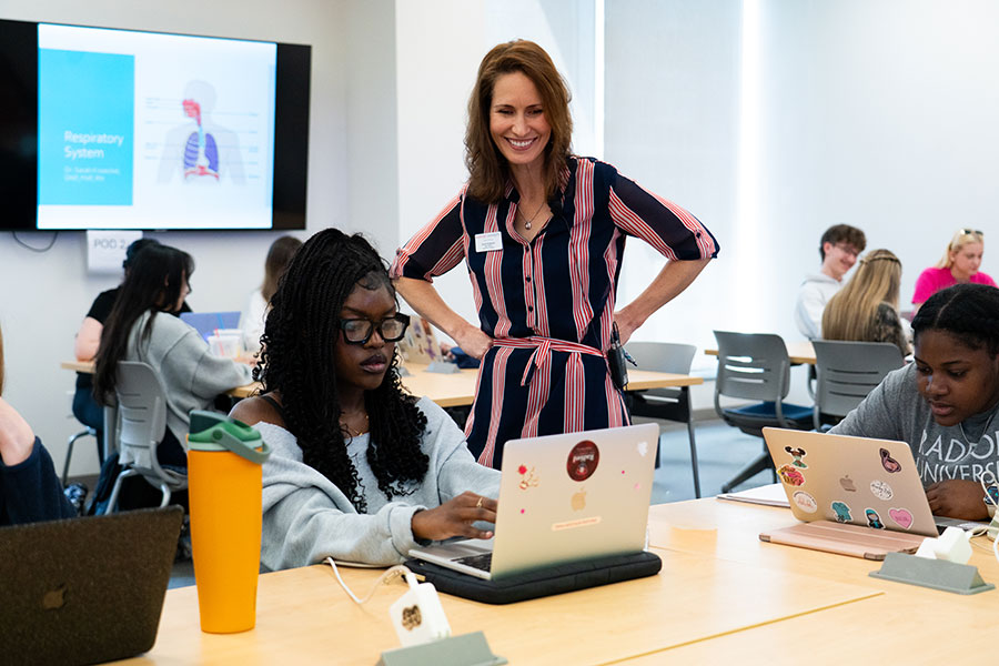 A Nursing faculty member works with a student on a laptop computer in a classroom
